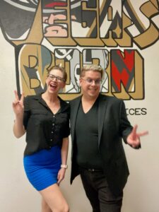 Dev and Zak throw up peace signs while standing in front of Vegas Born graffiti on an office the wall.