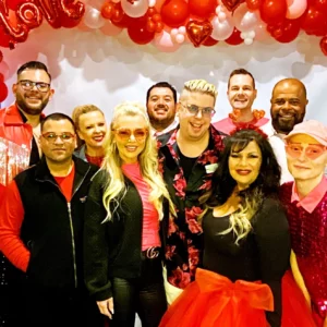 A group of people dressed in red surrounded by valetines day red balloons celebrates.