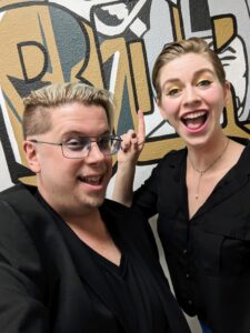 Zak and Dev laugh in a selfie photo. Both are dressed in black.