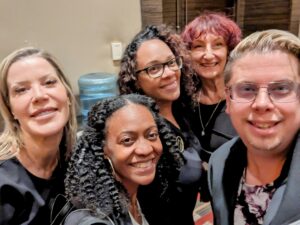 A group of five people huddle together for a selfie, they are all smiling.