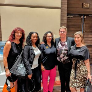 A group of five people pose in a convention area.