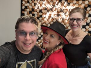 Zak, Leslie, and Dev stand in front of a gold and black flower wall.