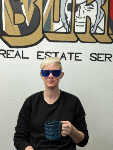 Tammi sitting at a table looking serious, she's wearing sunglasses and holding a coffee cup.